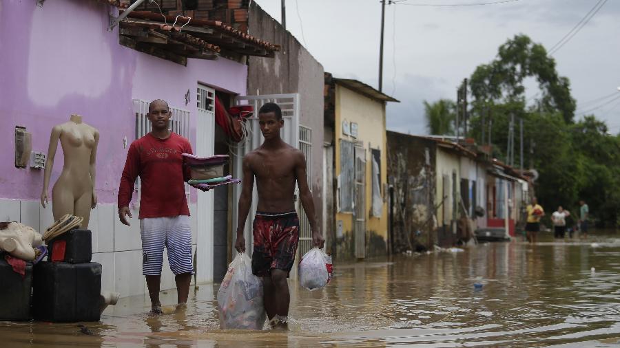 27.dez.2021 - Pessoas carregam seus pertences enquanto caminham na água após inundação em Itapetinga, Bahia - Xinhua/Lucio Tavara