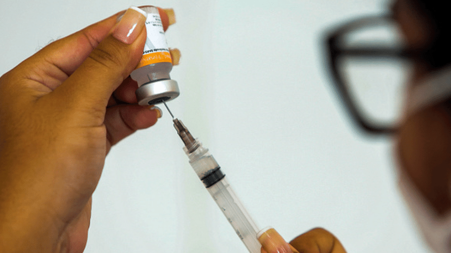 Profissional da saúde segura ampola de vacina e extrai líquido com uma agulha e seringa - Getty Images