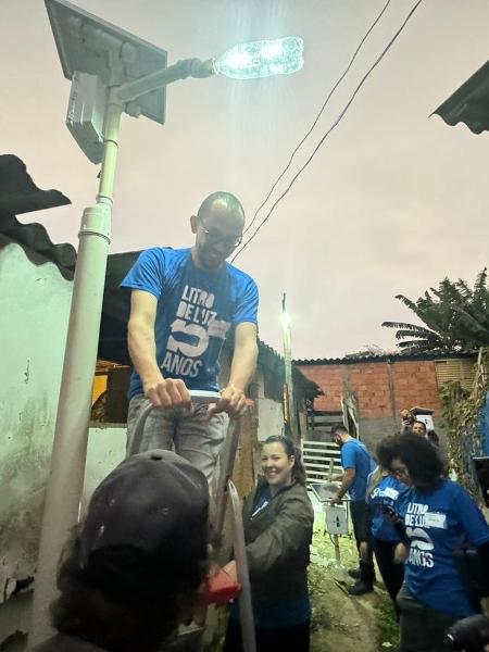 Voluntários participam de instalação de poste de luz movido à energia solar na comunidade Anchieta, na zona sul de São Paulo