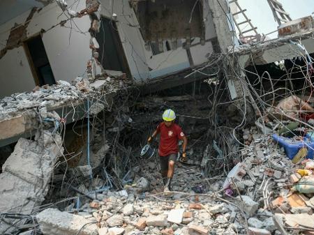 Um socorrista carrega equipamento enquanto uma equipe vasculha os escombros de um prédio destruído em busca de sobreviventes em Mandalay em 29 de março de 2025, um dia após um terremoto atingir o centro de Mianmar - SAI AUNG MAIN/AFP