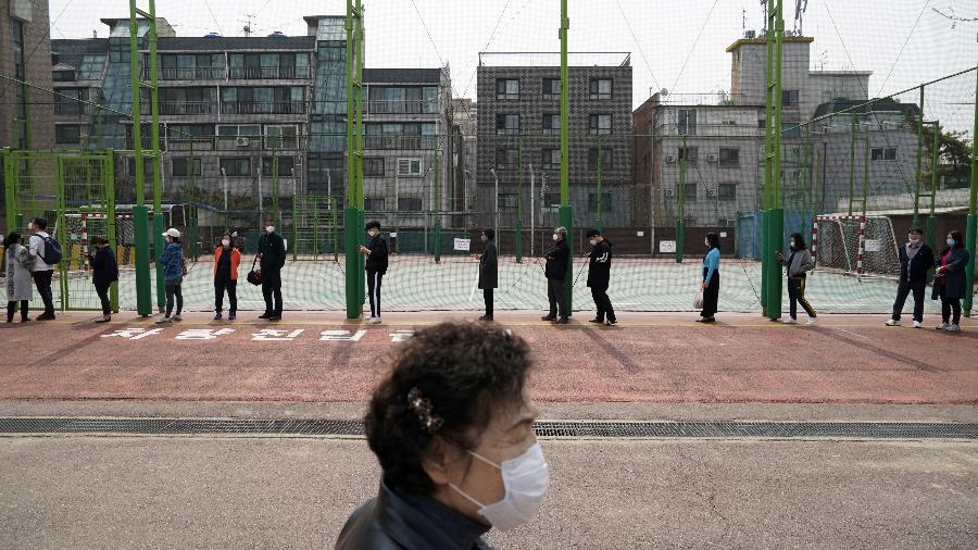 Uma mulher passa por uma fila de eleitores usando máscaras, em um esforço para impedir a propagação da doença por coronavírus, enquanto espera para votar em uma assembleia em Seul, Coréia do Sul - KIM HONG-JI/REUTERS