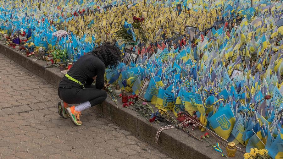 Mulher na Praça da Independência, em Kiev, decorada com bandeiras para lembrar de soldados mortos na guerra com a Rússia