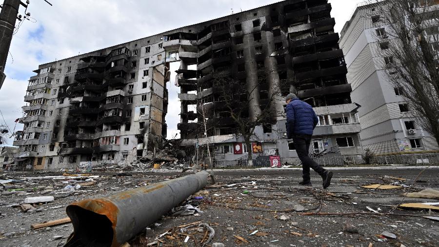 04.abr.2022/ Um homem passa por um fragmento de artilharia espalhado em uma rua enquanto passa por prédios destruídos na cidade de Borodianka, a noroeste de Kiev - SERGEI SUPINSKY / AFP