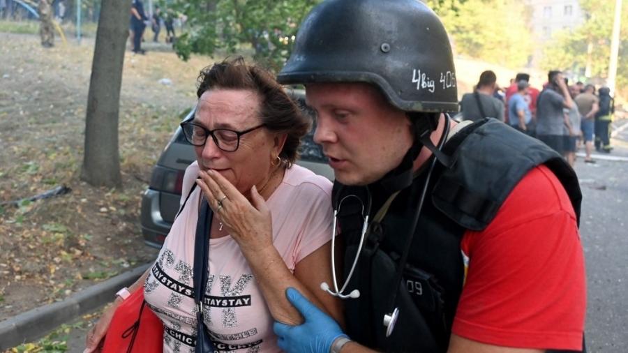 Um médico ucraniano ajuda uma mulher a deixar o local de um ataque com mísseis em Kharkiv em 15 de setembro de 2024 - SERGEY BOBOK/AFP