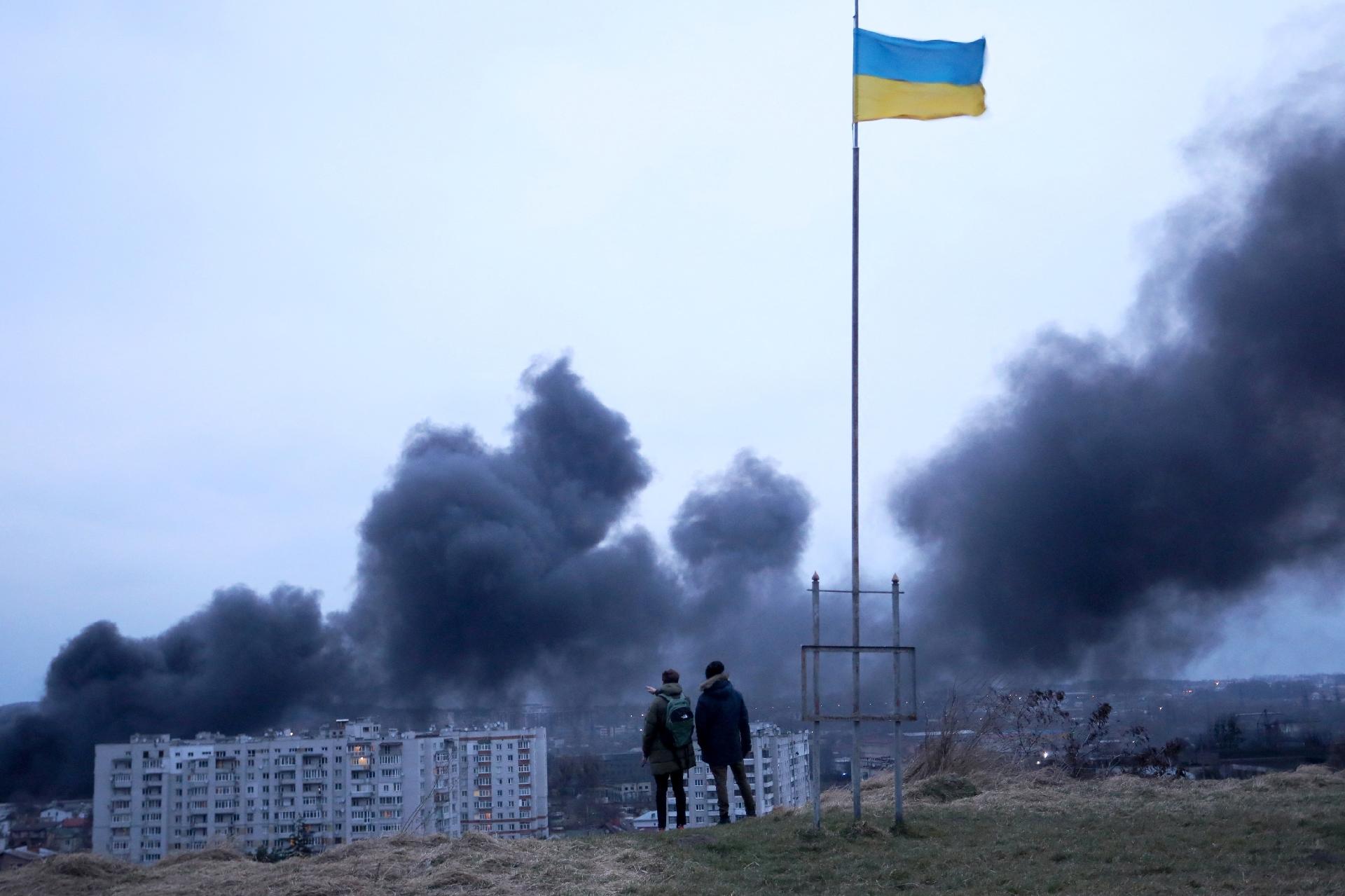March 26, 2022 - People standing next to the Ukrainian national flag watch the thick smoke rising after the airstrike on the city of Lviv in western Ukraine - March 26, 2022 - Aleksey Filipov/AFP