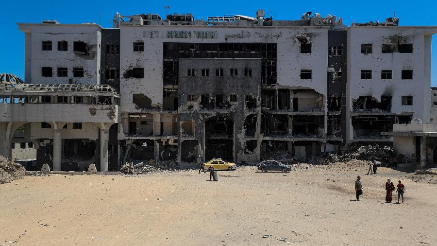 9.jul.2025 - Palestinos caminham ao lado de um prédio danificado no hospital Al-Shifa 9.jul.2025 - Palestinos caminham ao lado de um prédio danificado no hospital Al-Shifa