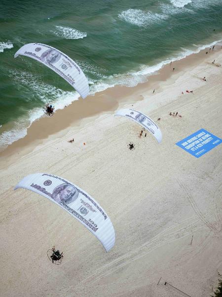 Seis parapentes sobrevoaram a capital fluminense, personalizados com notas gigantes de US$ 100