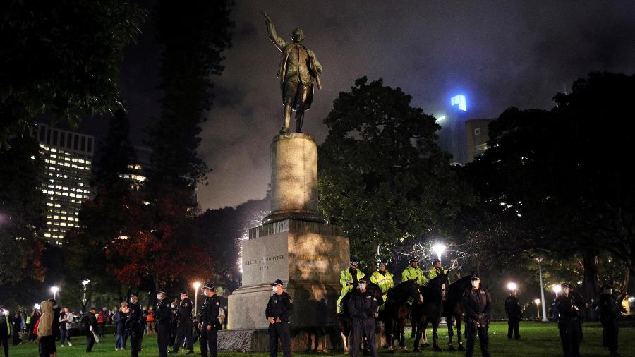 Policiais australianos vigiam a estátua de James Cook em Sydney, no último dia 11, para evitar a aproximação de manifestantes - Loren Elliott/Reuters