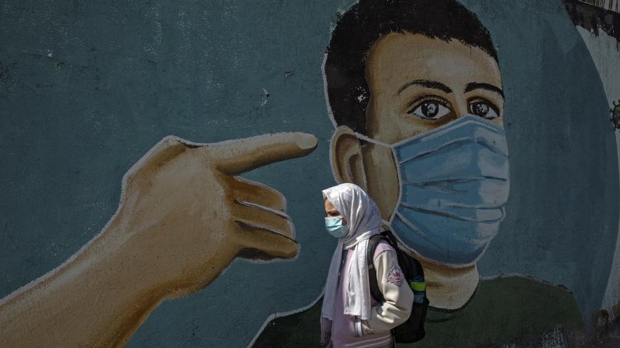 Menina passa por mural com o tema do coronavírus em Rafah, no sul da Faixa de Gaza - Said Khatib/AFP