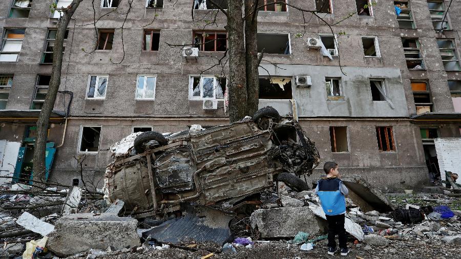 24.abr.2022 - Um menino fica ao lado de um veículo destruído em frente a um prédio de apartamentos danificado durante o conflito Ucrânia-Rússia na cidade portuária de Mariupol, no sul da Ucrânia - 24.abr.2022 - Alexander Ermochenko/Reuters
