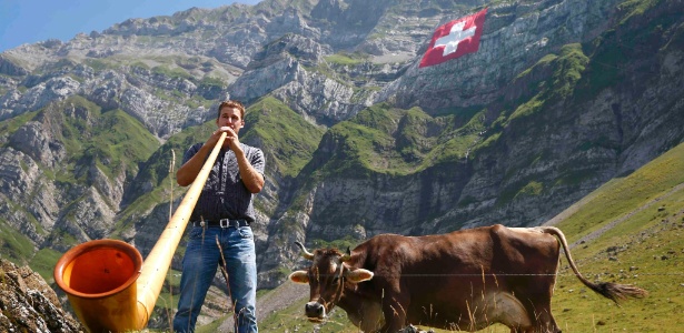 Homem toca espécie de berrante gigante ao lado da bandeira nacional e de uma vaca tradicional durante as comemorações do Dia Nacional da Suíça - Arnd Wiegmann - 31.jul.2015/Reuters