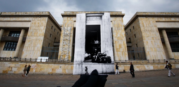 Uma pessoa segura uma fotografia histórica dos soldados ingressando no Palácio de Justiça com um tanque, diante do Palácio de Justiça em Bogotá, na Colômbia - Mauricio Alvarado/Colprensa/Xinhua