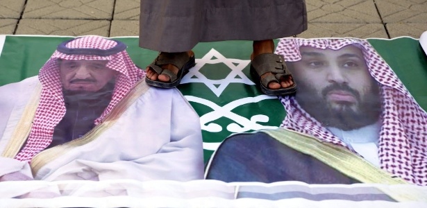 Homem do movimento xiita houthi pisa em bandeira com a imagem do rei saudita, Salman bin Abdelaziz, e de seu filho durante um protesto na embaixada saudita em Sanaa, no Iêmen