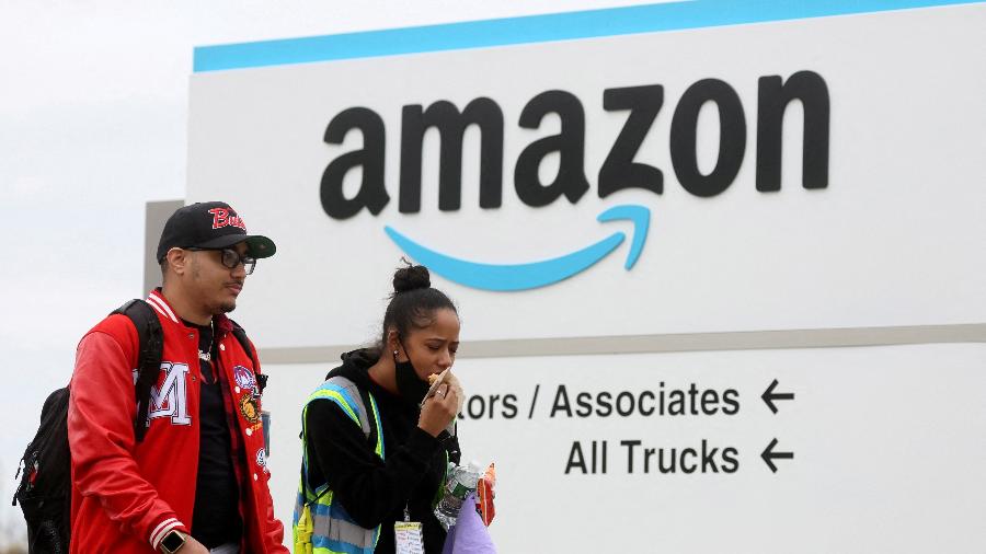 Funcionários da Amazon caminham próximo de logotipo da empresa em armazém em Nova York - Brendan McDermind/Reuters
