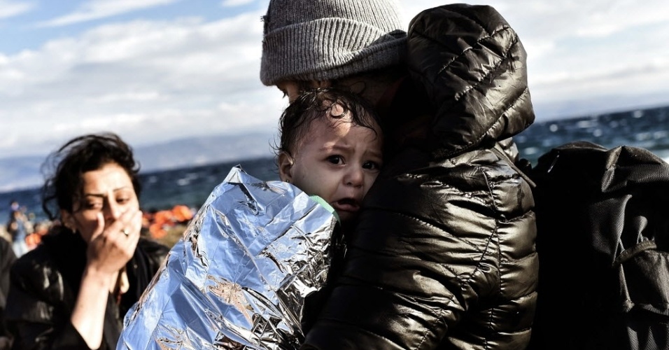 30.set.2015 - Bebê chora ao ser segurado por homem na ilha grega de Lesbos. Refugiados atravessaram o mar Egeu de bote da Turquia até a Grécia