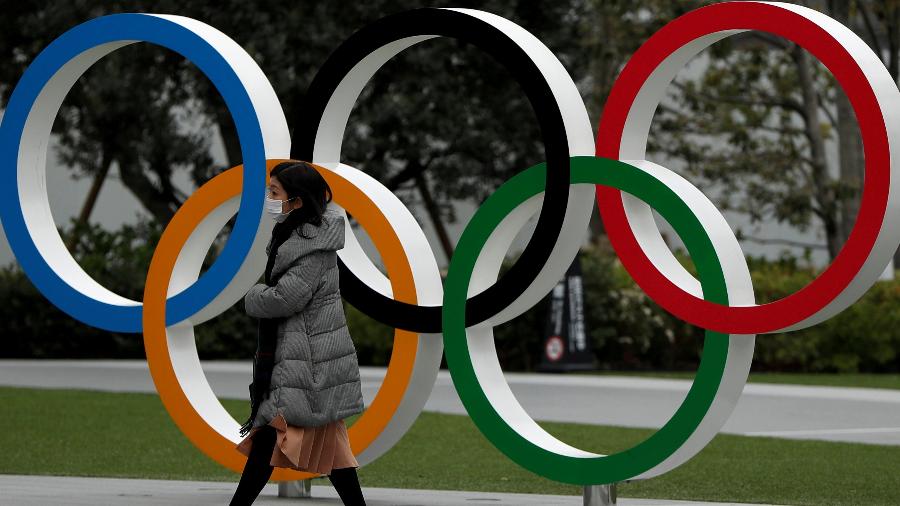 Mulher com máscara passa pelos anéis olímpicos em Tóquio - Issei Kato