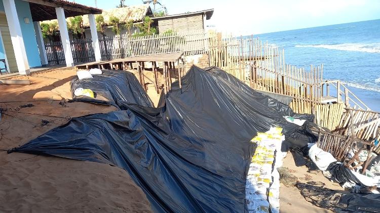 Casa protegida por lona e sacos de areia na praia de Peroba, em Icapuí (CE)