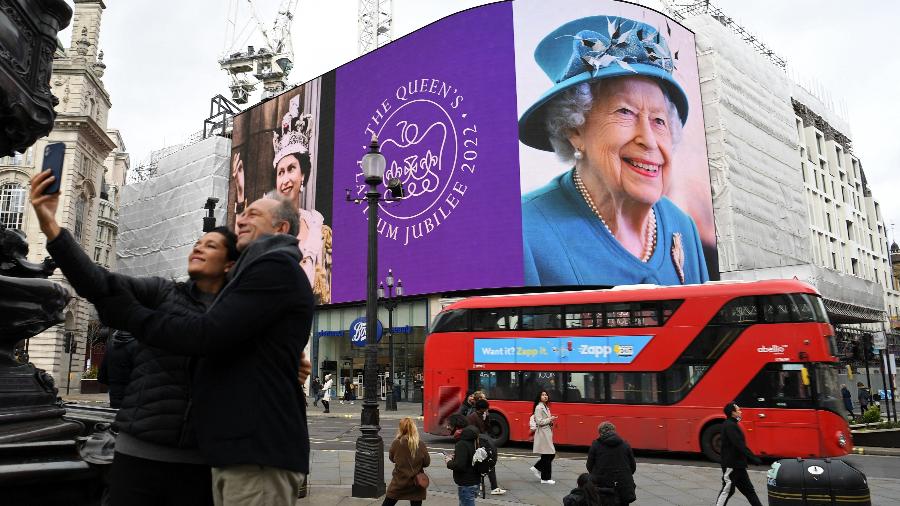 Um casal tira uma selfie enquanto imagens da rainha britânica Elizabeth II são exibidas nas grandes telas digitais em Piccadilly Circus, no centro de Londres, em 6 de fevereiro de 2022, para marcar o início do Ano do Jubileu de Platina da Rainha - DANIEL LEAL/AFP