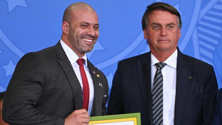 Deputado Daniel Silveira posa ao lado do presidente Jair Bolsonaro (d) segurando uma cópiado do indulto presidencial que recebeu - Evaristo Sá/AFP