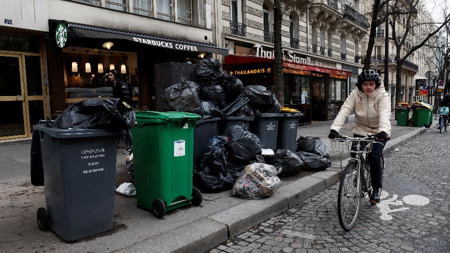 Pessoas são vistas em uma rua onde latas de lixo estão transbordando, pois o lixo não foi coletado, em Paris, em 10 de março - BENOIT TESSIER/REUTERS