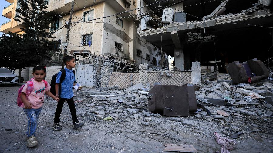 03.out.26 - Crianças palestinas passam pelo local de um ataque israelense a um prédio de apartamentos na Cidade de Gaza