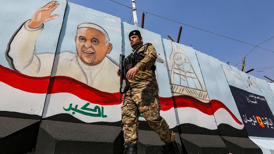 1.mar.2021 - Militar iraquiano caminha armado em frente a um mural com a imagem do papa Francisco em Bagdá, no Iraque - Sabah Arar/AFP