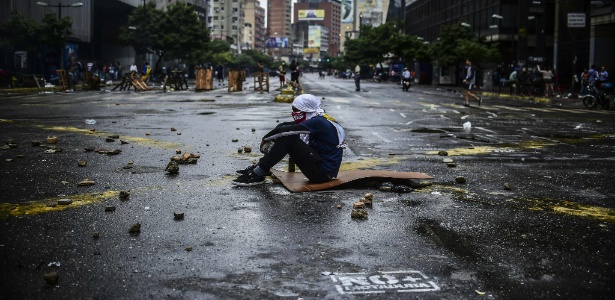 Manifestante da oposição senta no asfalto durante protesto contra o governo de Nicolás Maduro, em Caracas - Ronaldo Schemidt/ AFP