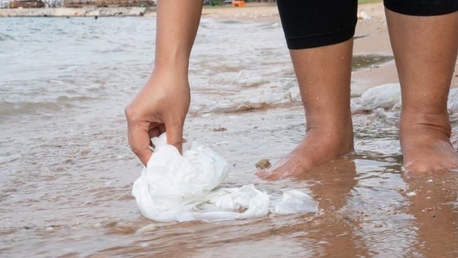 Pessoa com os pés em ná agua retirando lixo da beirada do rio - Getty Images