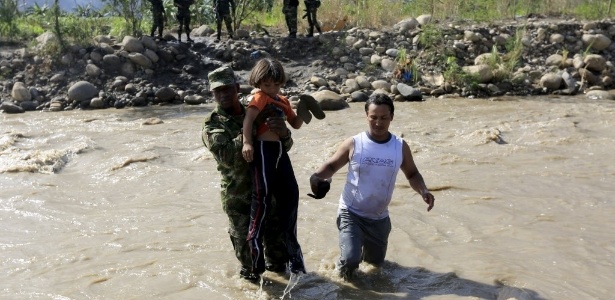 Soldado colombiano ajuda um pai e uma criança a atravessarem o rio Táchira, de volta para a Colômbia - Jose Miguel Gomez/Reuters