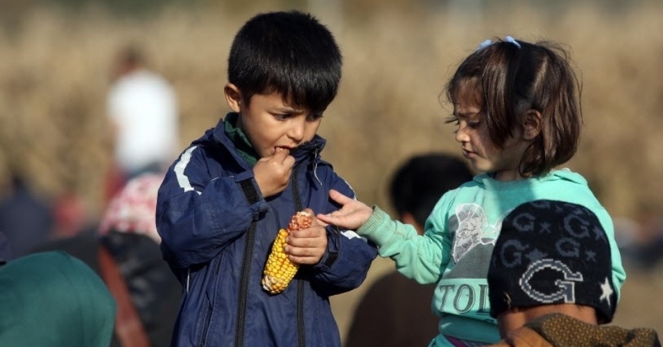 27.out.2015 - Em local próximo à cidade de Rigonce, na Eslovênia, crianças refugiadas comem milho enquanto esperam o grupo de imigrantes do qual fazem parte seguir caminho rumo à fronteira com a Croácia
