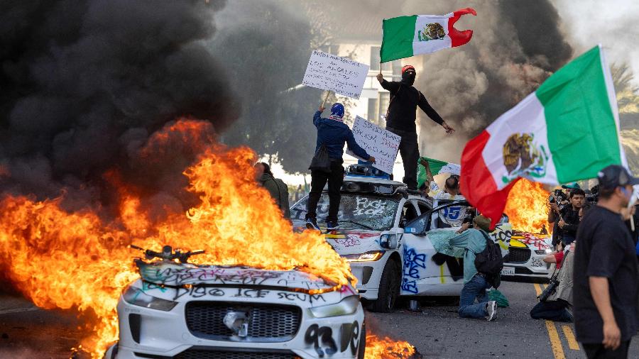 Manifestantes posam sobre carros autônomos, da Wayme, que foram incendiados em Los Angeles, na Califórnia (EUA) - Ringo Chiu/AFP