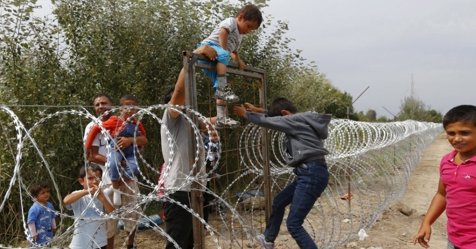 25.ago.2015 - Imigrantes sírios escalam cerca de arame farpado na fronteira entre a Sérvia e a Hungria. O governo húngaro iniciou a construção de uma cerca de 175 quilômetros para conter o fluxo de imigrantes