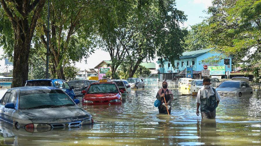 21.dez.21 - Pessoas caminham em enchente na cidade de Selangor após fortes chuvas que deixaram pelo menos 14 mortos e mais de 70.000 desabrigados na Malásia - ARIF KARTONO/AFP