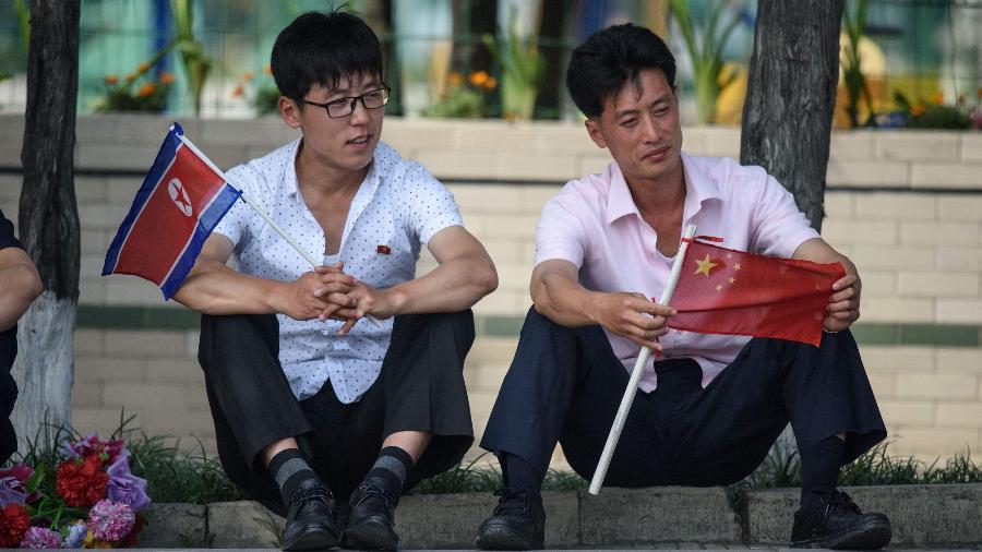 Dois homens seguram a bandeira da Coreia do Norte e da China, respectivamente, a espera da visita do presidente da China, Xi Jinping - Ed JONES / AFP