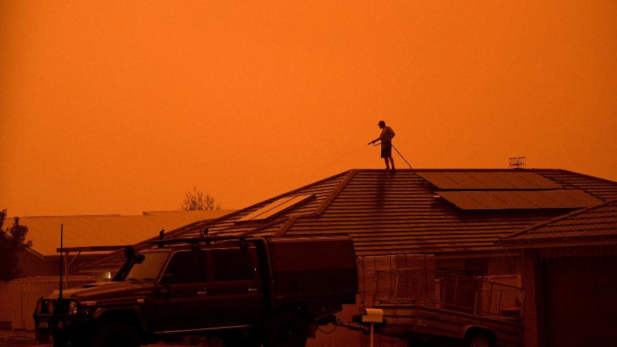 4.jan.2020 - Homem usa mangueira para molhar o telhado de casa em Nowra, em Nova Gales do Sul, na Austrália - Tracey Nearmy/Reuters