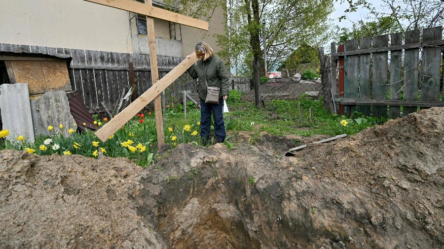  Lyudmyla Kizilova, 67 anos, observa a cova onde o corpo de seu marido foi encontrado, em Bucha - Sergei SUPINSKY / AFP