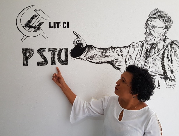 Vera Lúcia à frente de desenho na parede que mostra Leon Trotsky e o logo da 4ª Internacional