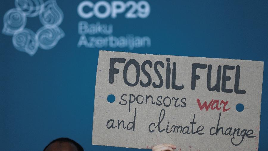 Ativista ambiental segura cartaz para protestar contra o uso de combustíveis fósseis durante a COP29, em Baku, no Azerbaijão