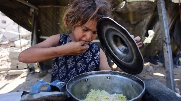 Menina palestina come arroz distribuído por cozinha solidária em Gaza