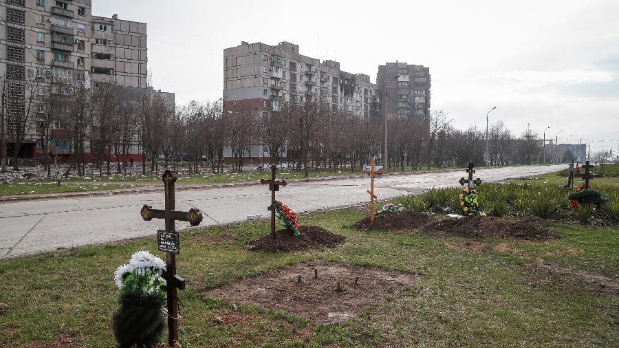 10.abr.2022 - Túmulos de civis mortos durante o conflito Ucrânia-Rússia são vistos ao lado de prédios de apartamentos na cidade portuária de Mariupol, no sul da Ucrânia - 10.abr.2022 - Alexander Ermochenko/Reuters