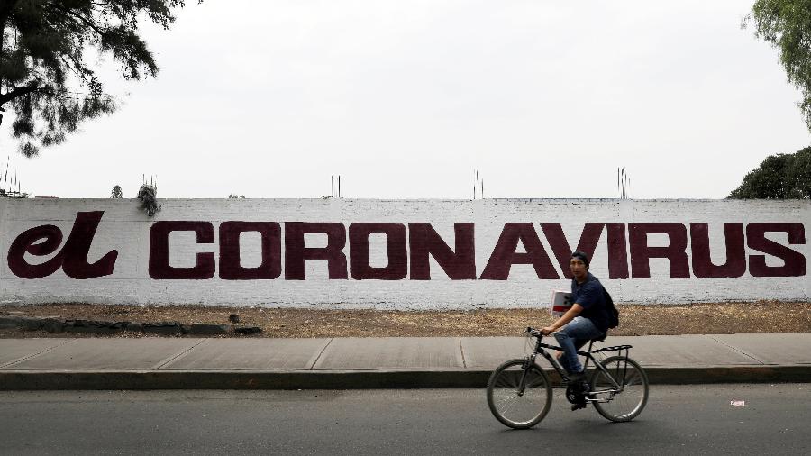 Pintura escrita coronavírus é vista em um muro enquanto um homem passa de bicicleta na Cidade do México - CARLOS JASSO/REUTERS