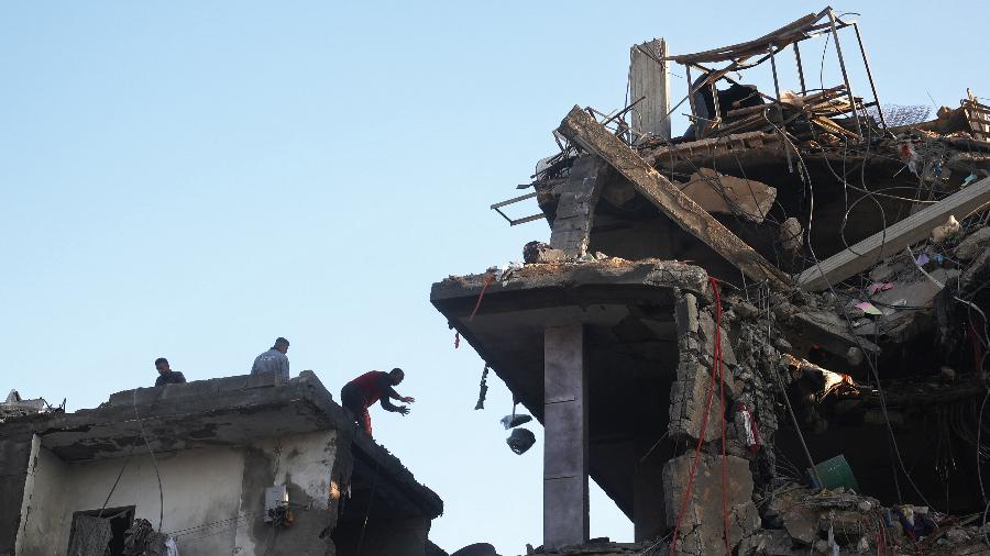 Pessoas procuram seus pertences entre escombros de edifício destruído após ataque em campo de refugiados na Faixa de Gaza