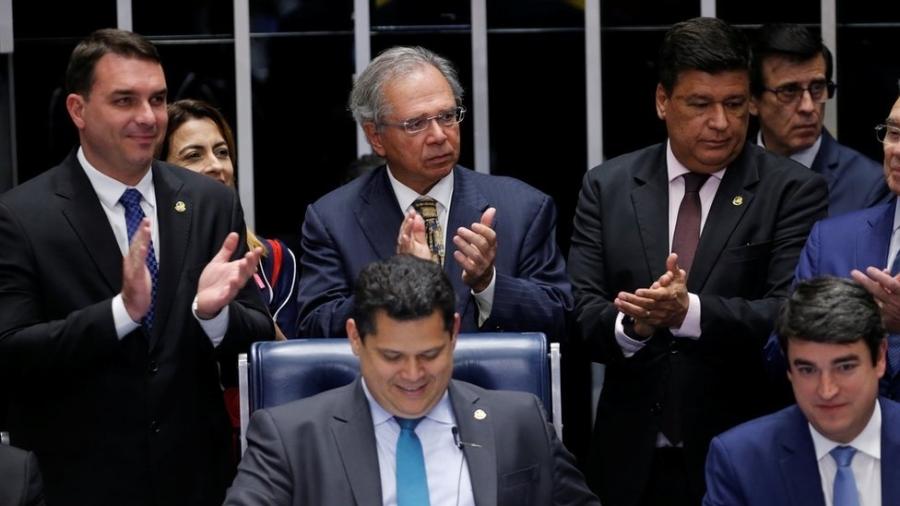 O senador Flávio Bolsonaro, o ministro Paulo Guedes (na foto, os dois à esquerda e em pé) e o presidente da Casa, Davi Alcolumbre (sentado, ao centro), entre outros, comemoram aprovação de texto-base no Senado - Adriano Machado/Reuters