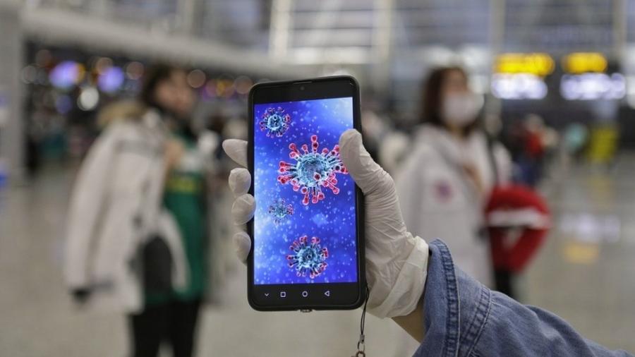 Passageiro mostra ilustração do coronavírus em seu celular no aeroporto de Guangzhou, na província chinesa de Guangdong - EPA
