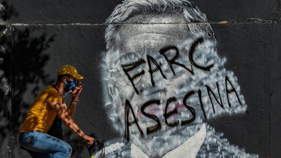 5.set.2020 - Homem de bicicleta passa por mural contra as FARC e o ex-presidente colombiano Álvaro Uribe  - Juan Barreto/AFP