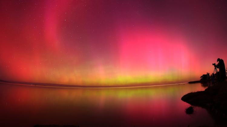 Um fotógrafo tira fotos da Aurora Boreal sobre as águas do Lago Ellesmere, na Nova Zelândia