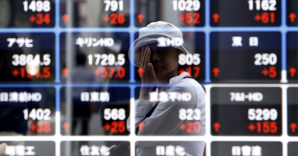 27.ago.2015 - Pedestre é refletida em um painel eletrônico que mostra os preços das ações em uma corretora em Tóquio, no Japão