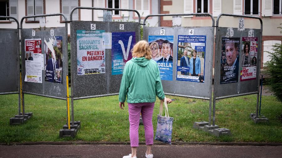 30.jun.2024 - Pedestre olha cartazes eleitorais para as eleições legislativas da França em Wissembourg, leste da França. Um país dividido está votando em eleições parlamentares de alto risco que podem levar o partido anti-imigrante e eurocético de Marine Le Pen a chegar ao poder em uma estreia histórica