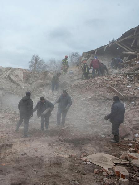 Pessoas removem destroços no local de um edifício de base militar que, segundo as forças terrestres ucranianas, foi destruído por um ataque aéreo, na cidade de Okhtyrka, na região de Sumy - Imprensa ucraniana/Via Reuters