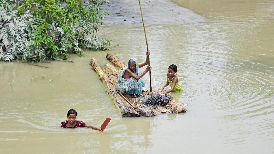 21.jul.2019 - Mulher faz uma balsa improvisada enquanto meninas atravessam as águas da inundação na aldeia de Laharighat, no distrito de Morigaon, no estado de Assam, na Índia - Anuwar Hazarika/Reuters
